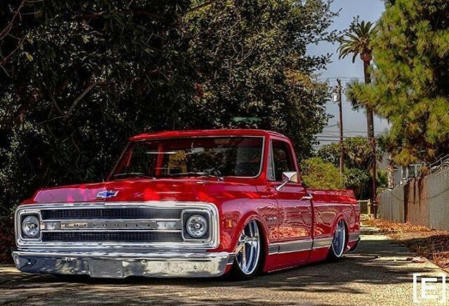 Red vintage pickup truck parked on a sunny street with trees.