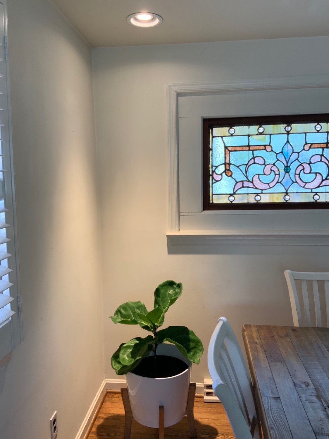 Indoor plant in white pot beside wooden table and stained glass window.
