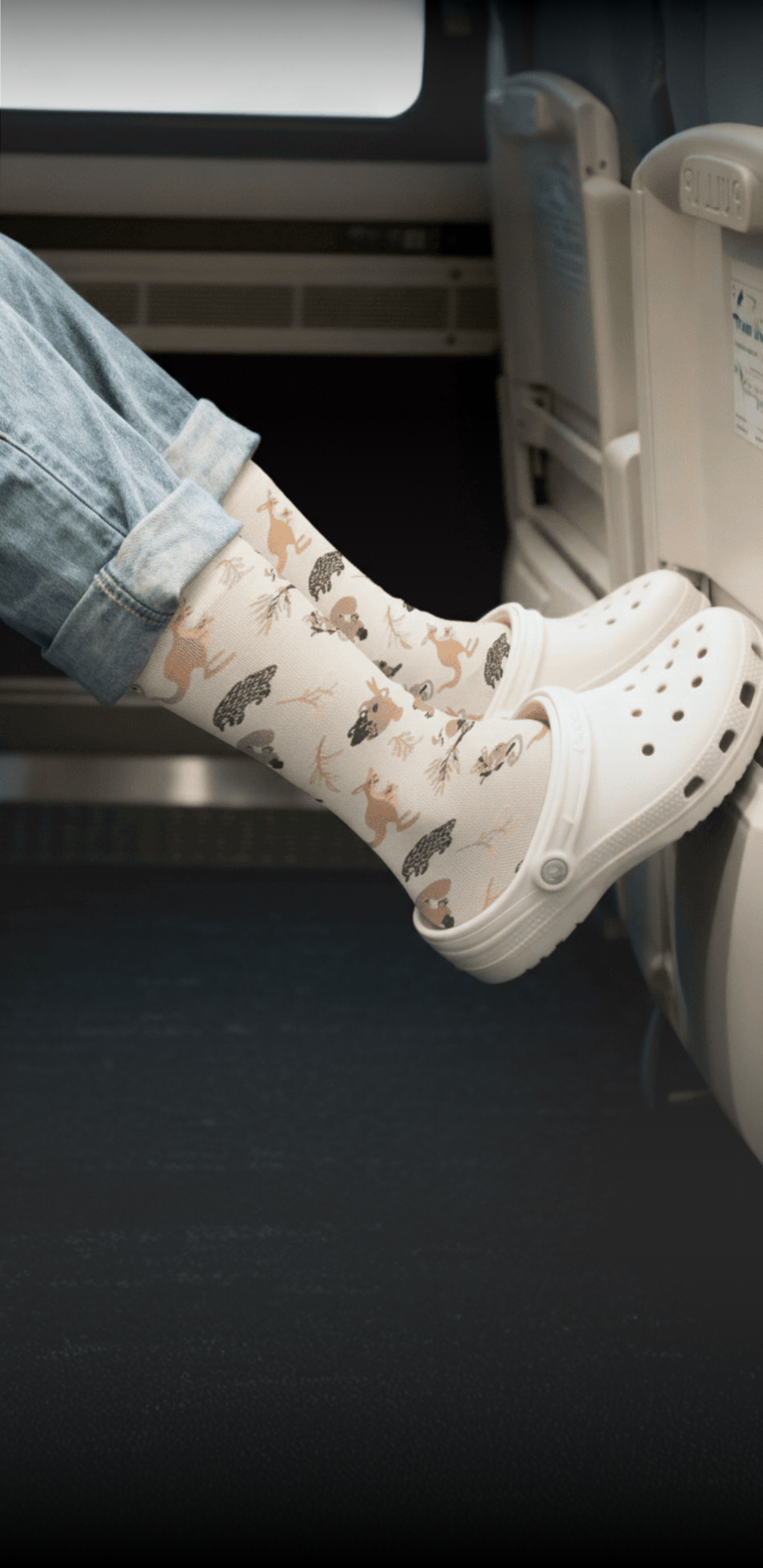 Person wearing animal-patterned socks and white clogs rests feet on a seat.