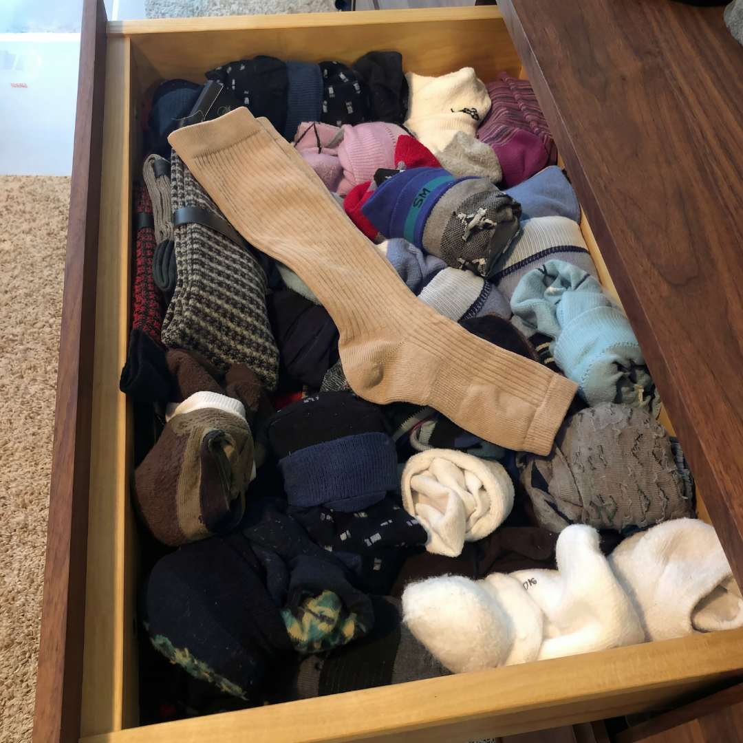 An open wooden drawer filled with many pairs of socks, with one unfolded on top.