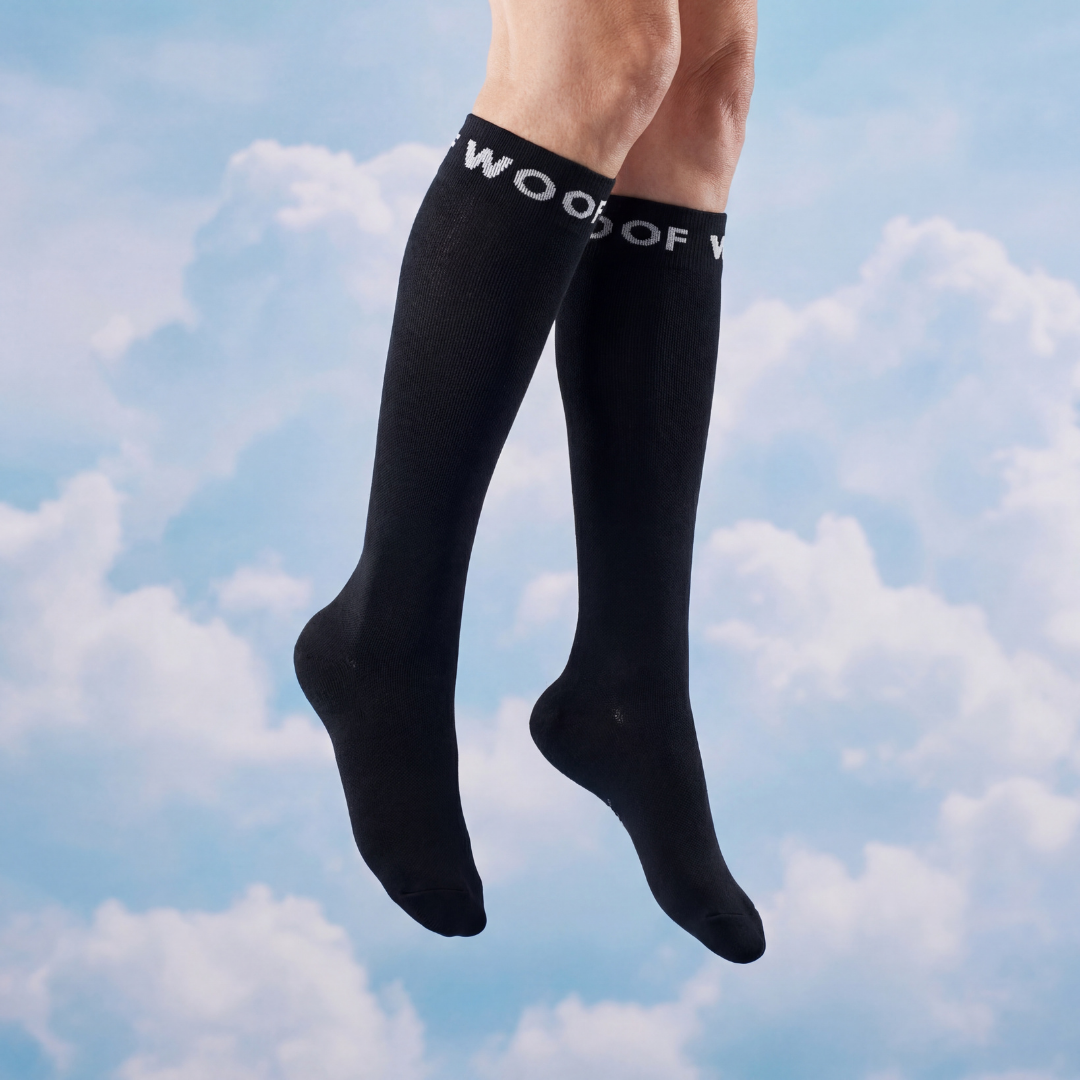 A person's legs wearing black knee-high socks with white lettering at the top against a cloudy sky background.