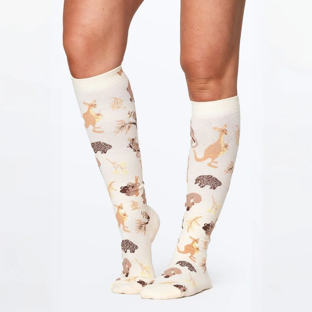 A person wearing off-white knee-high socks with a repeating pattern of Australian animals.