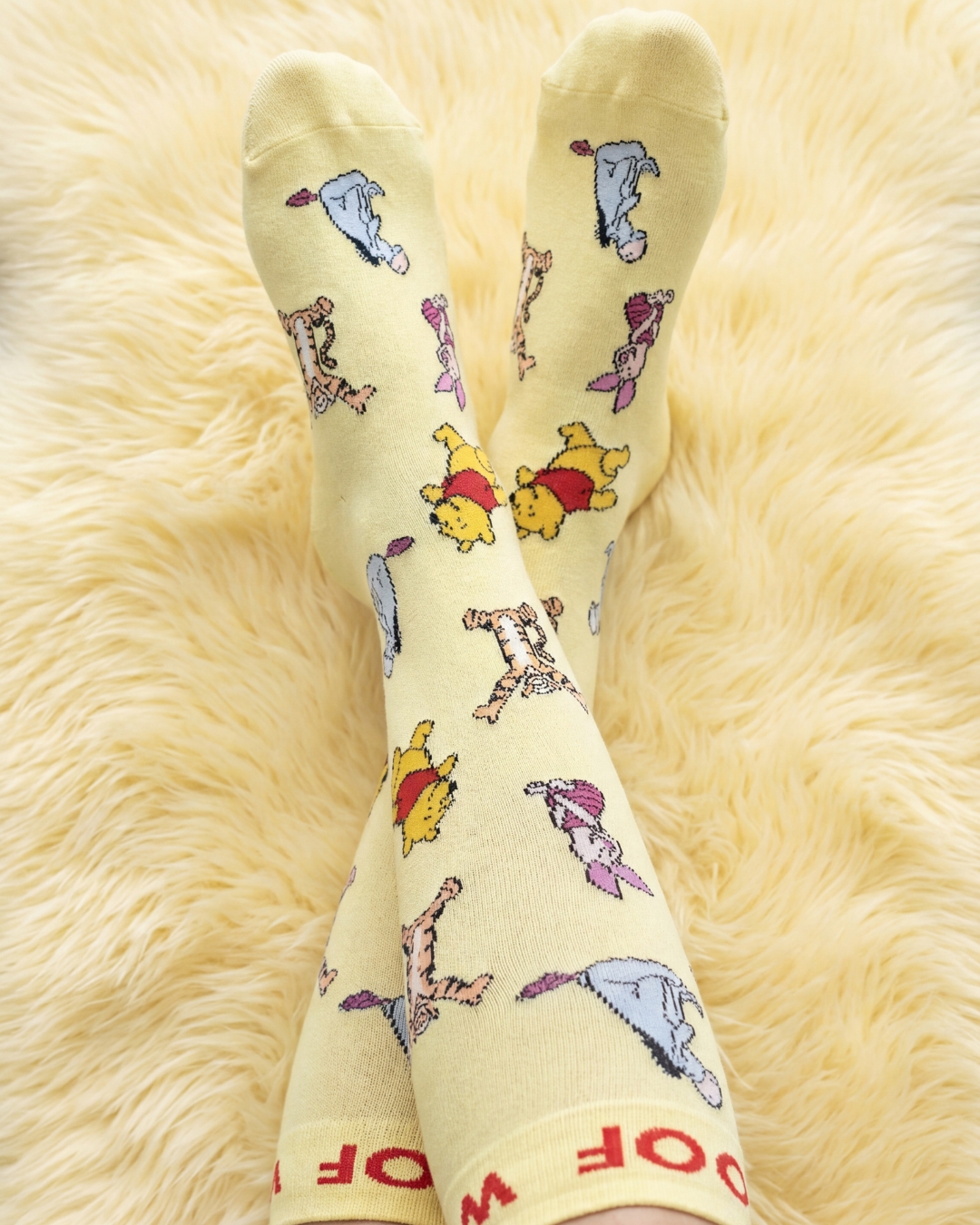 Feet in yellow Winnie the Pooh socks resting on a fluffy yellow rug