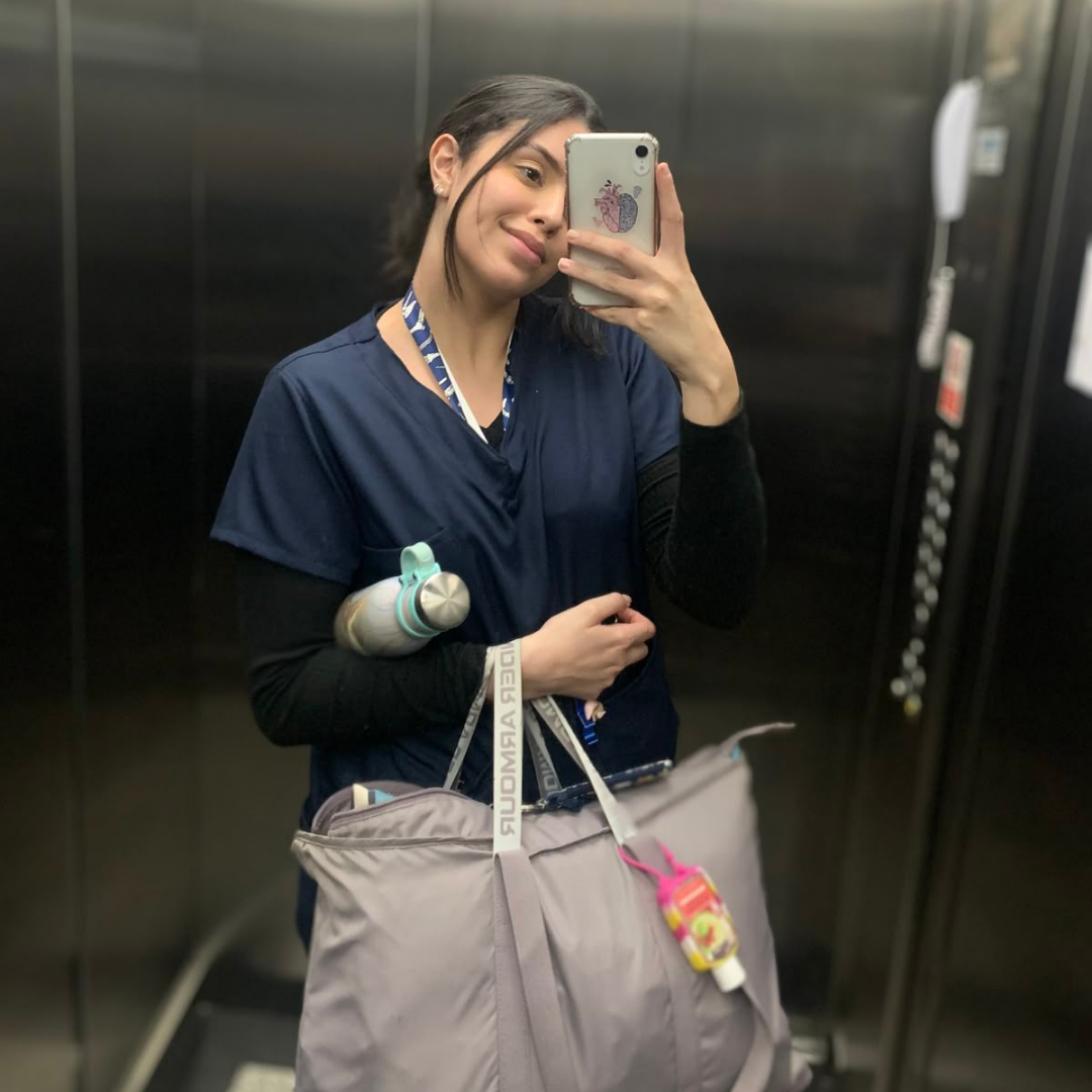 Person in scrubs taking a mirror selfie in an elevator.
