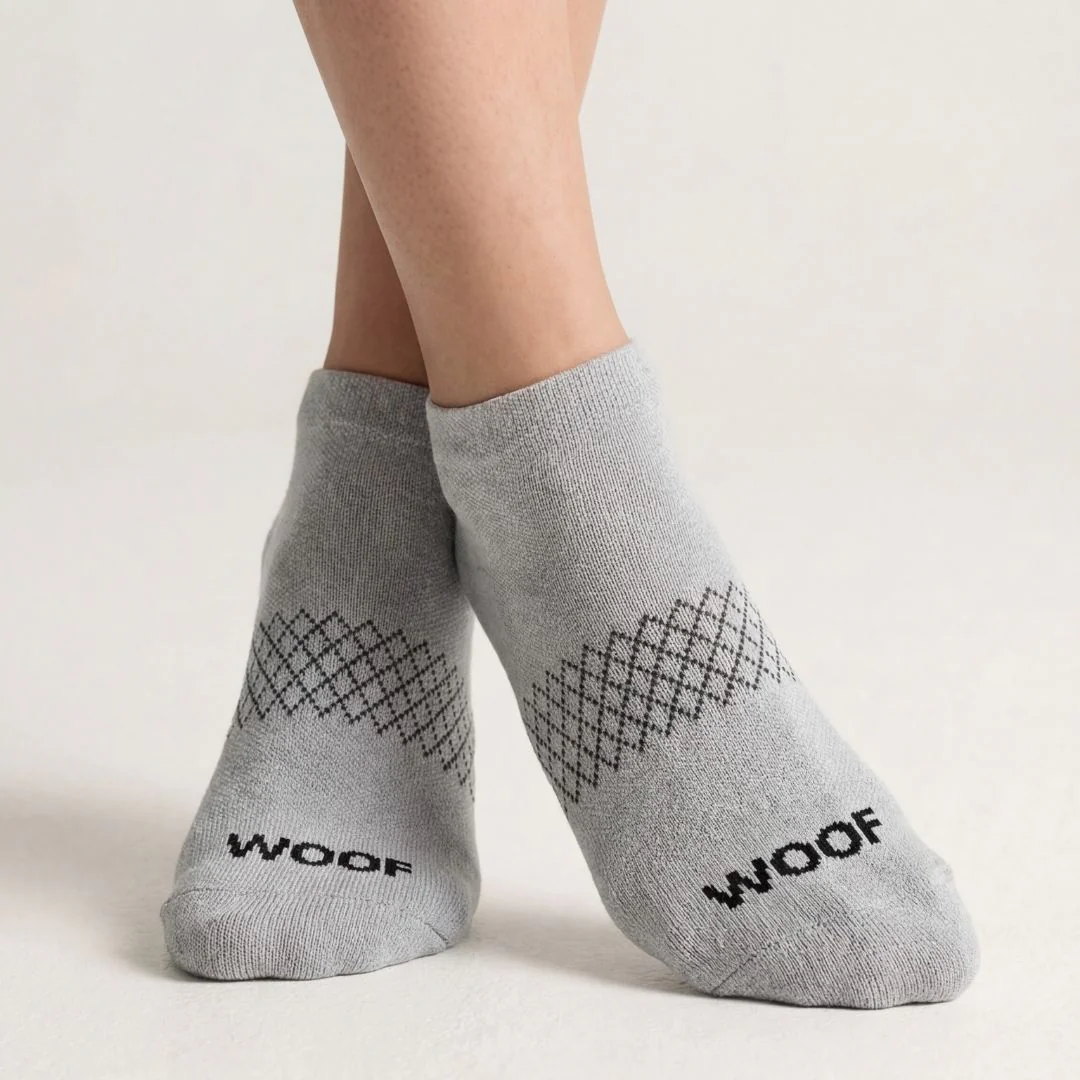 A pair of feet wearing light grey ankle socks with a diamond pattern and the word 'WOOF'.