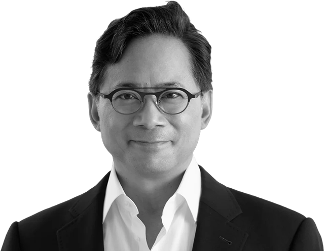 A man wearing glasses and a suit smiles in a black and white photo.