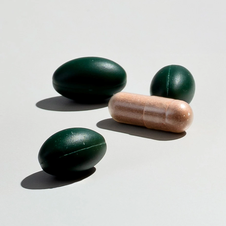 Three green capsules and one brown pill on a plain background.