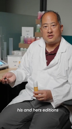 Person in lab coat holding a product, with laboratory equipment in the background.