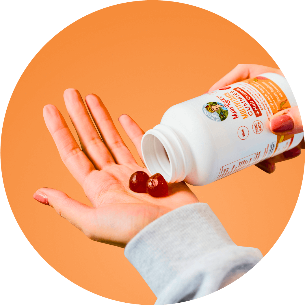 Hand holding gummy vitamins from a white bottle against an orange background.