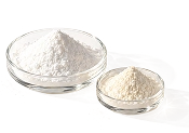 A large glass bowl of white powder next to a smaller glass bowl of off-white powder.