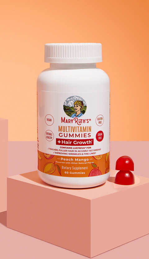 Bottle of multivitamin gummies with two red gummies beside it on a peach background.