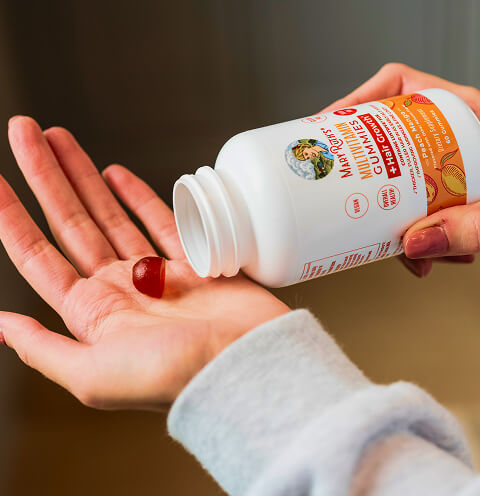 Hand holding a gummy from a vitamin bottle.