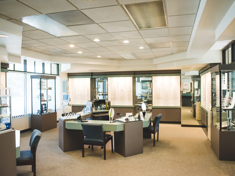 The interior of an optical store with eyeglass displays and a central fitting desk.