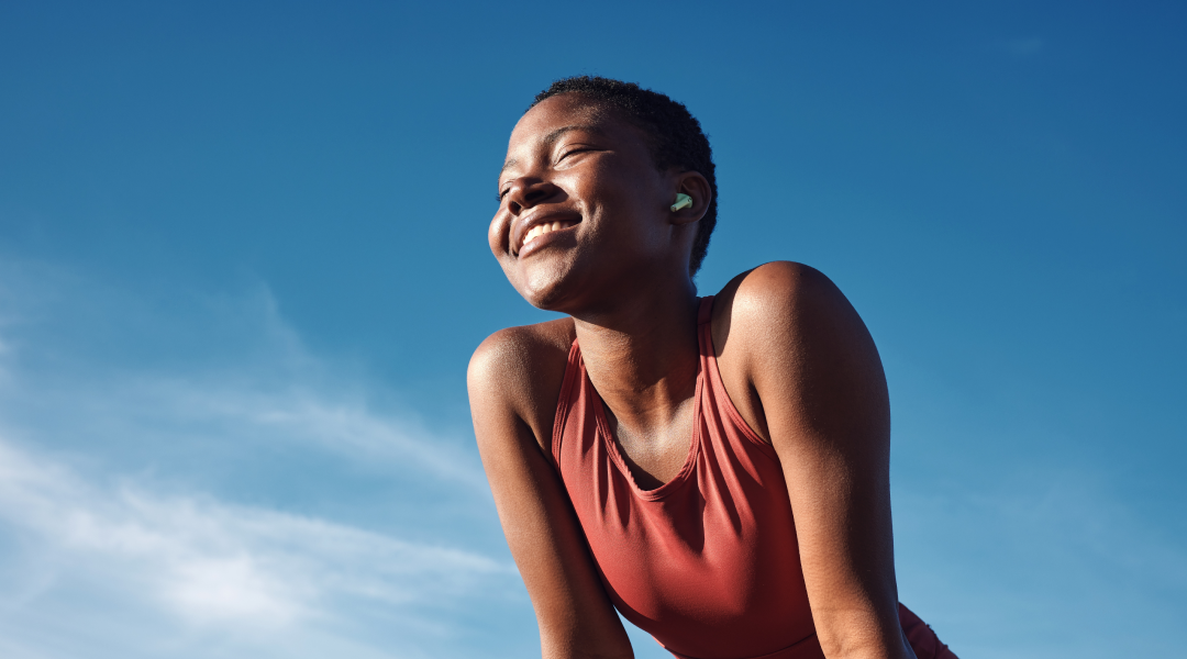 Person smiling outdoors under a clear blue sky.