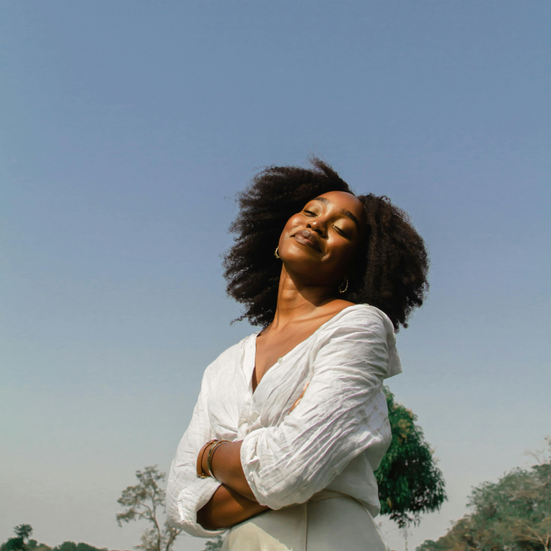 Woman in white shirt smiling with eyes closed against a clear blue sky.