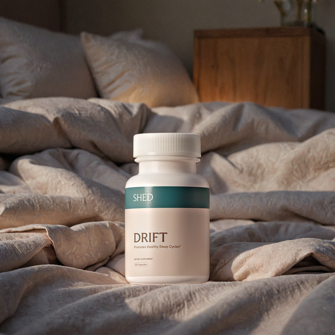 A bottle labeled 'Drift' on a rumpled bed with pillows.