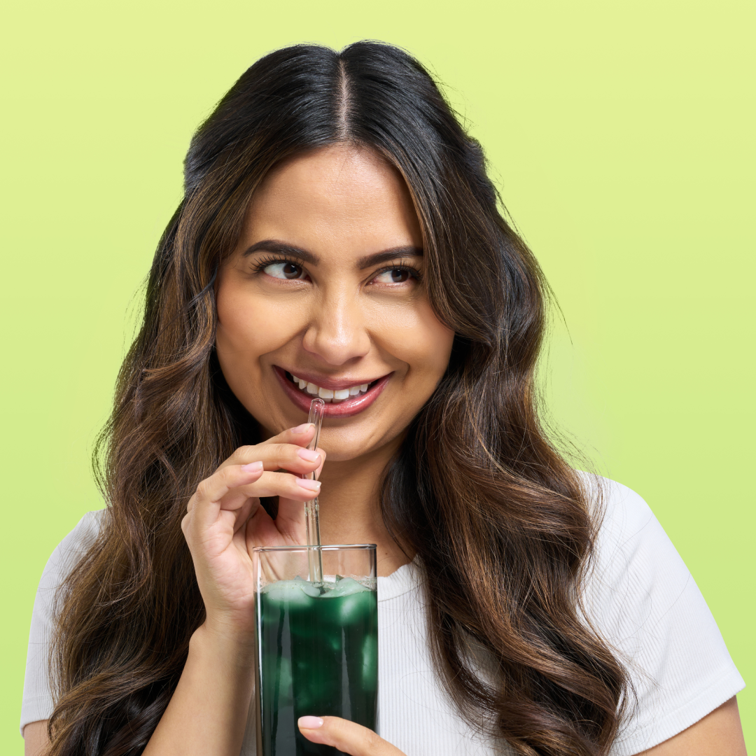 Woman smiling while drinking a green beverage with a straw.