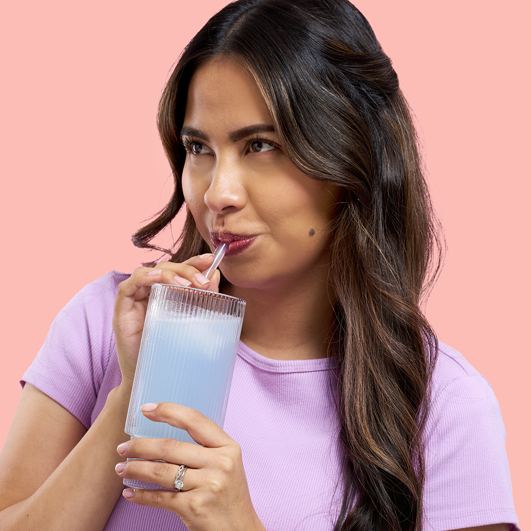 Woman in purple shirt drinking from a glass with a straw.