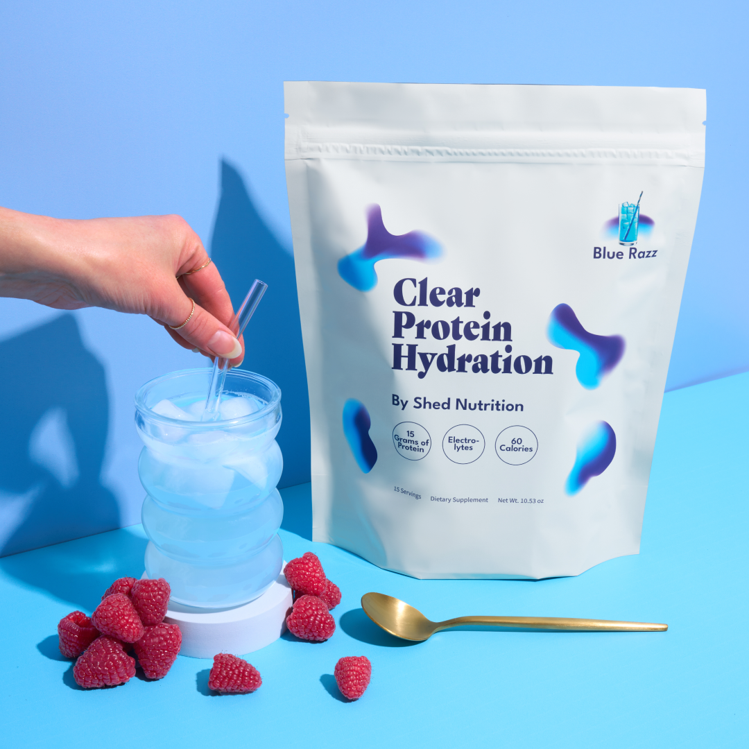 Hand holding a glass with blue drink, raspberries, and protein powder bag.