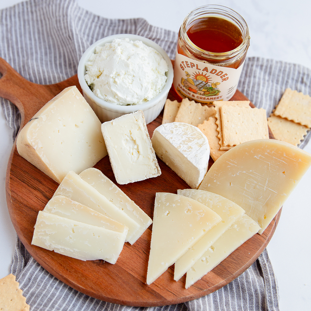 Cheese platter with crackers, dark chocolate, and a jar of spread on a wooden board.