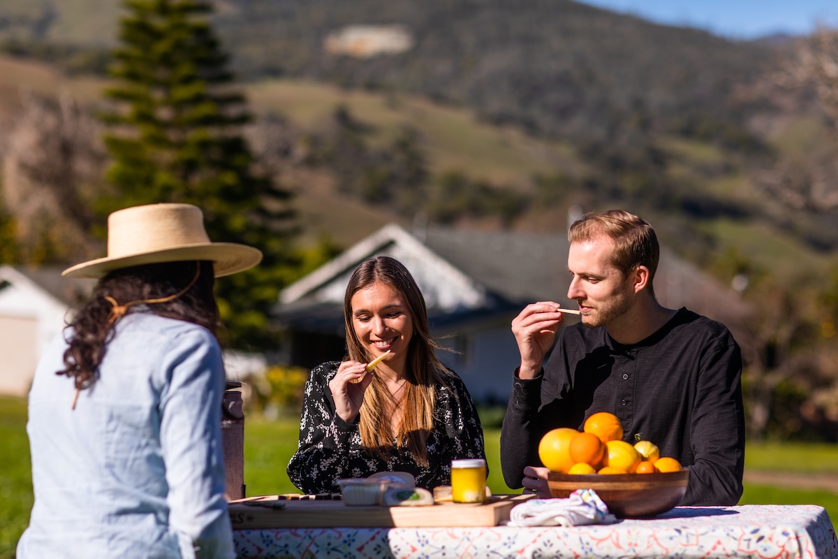 Three people enjoying a picnic with fruit and snacks outdoors.