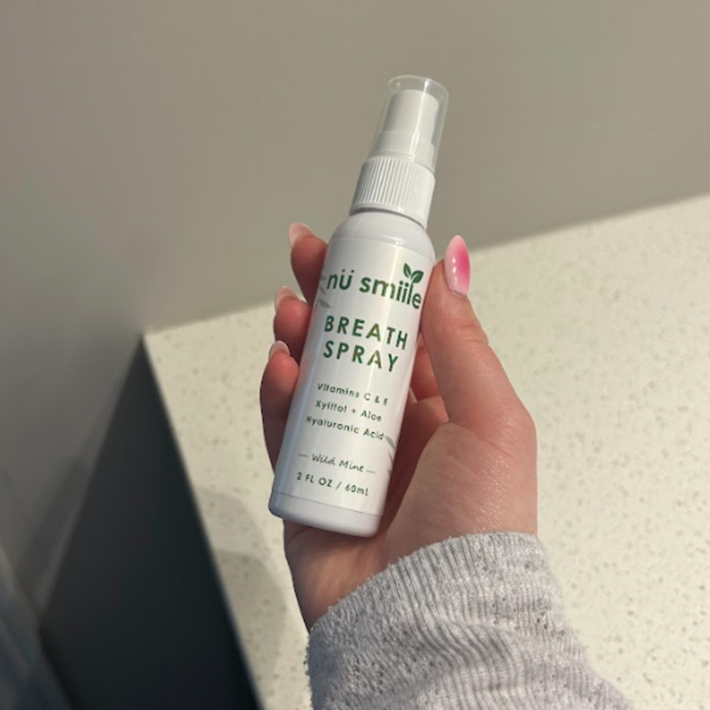 Hand holding a bottle of breath spray labeled 'nü smiile.'