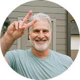 Smiling man making a peace sign with his hand outdoors.