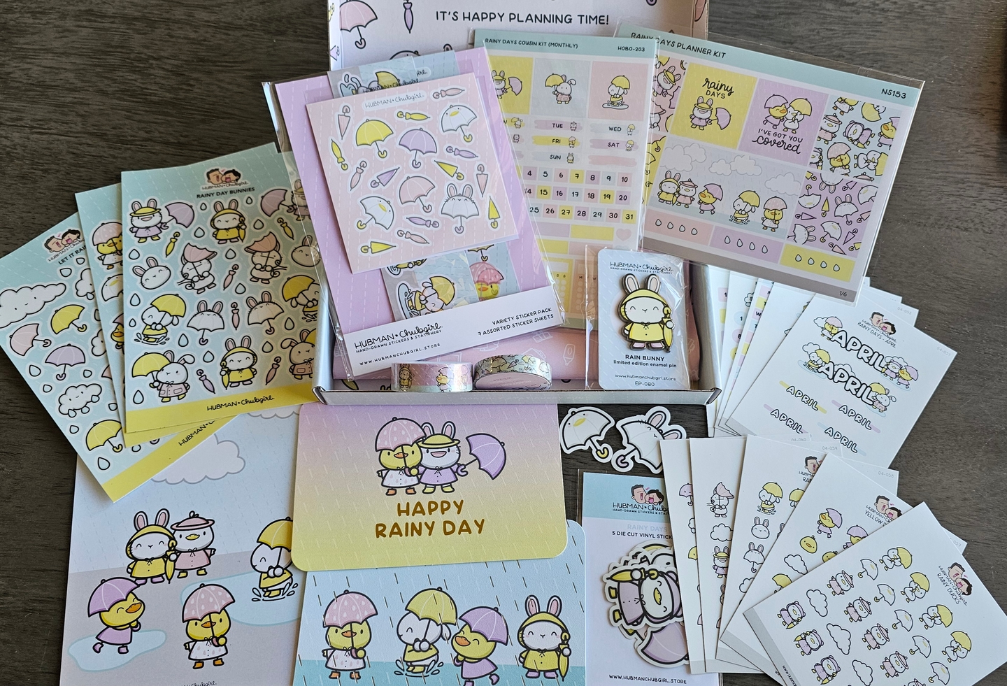 A collection of rainy day themed stationery, including stickers, cards, an enamel pin, and washi tape.