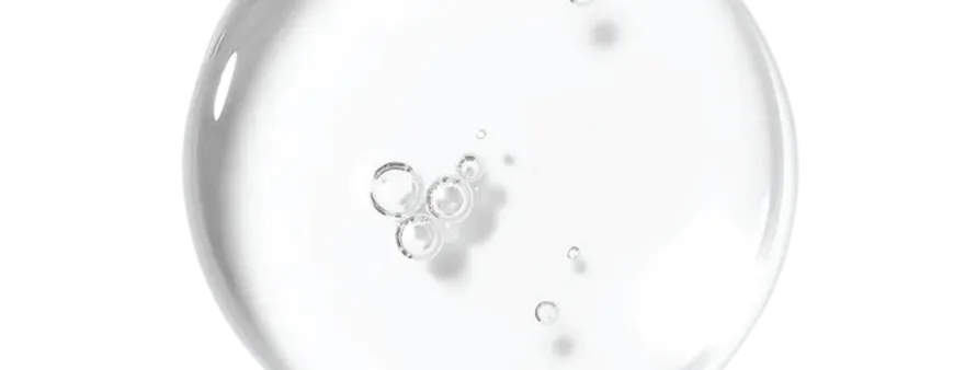 A close-up of a clear, round drop of liquid with bubbles inside, against a solid green background.