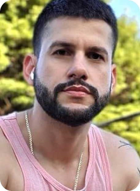 Person with beard and earphones, wearing a pink tank top outdoors.