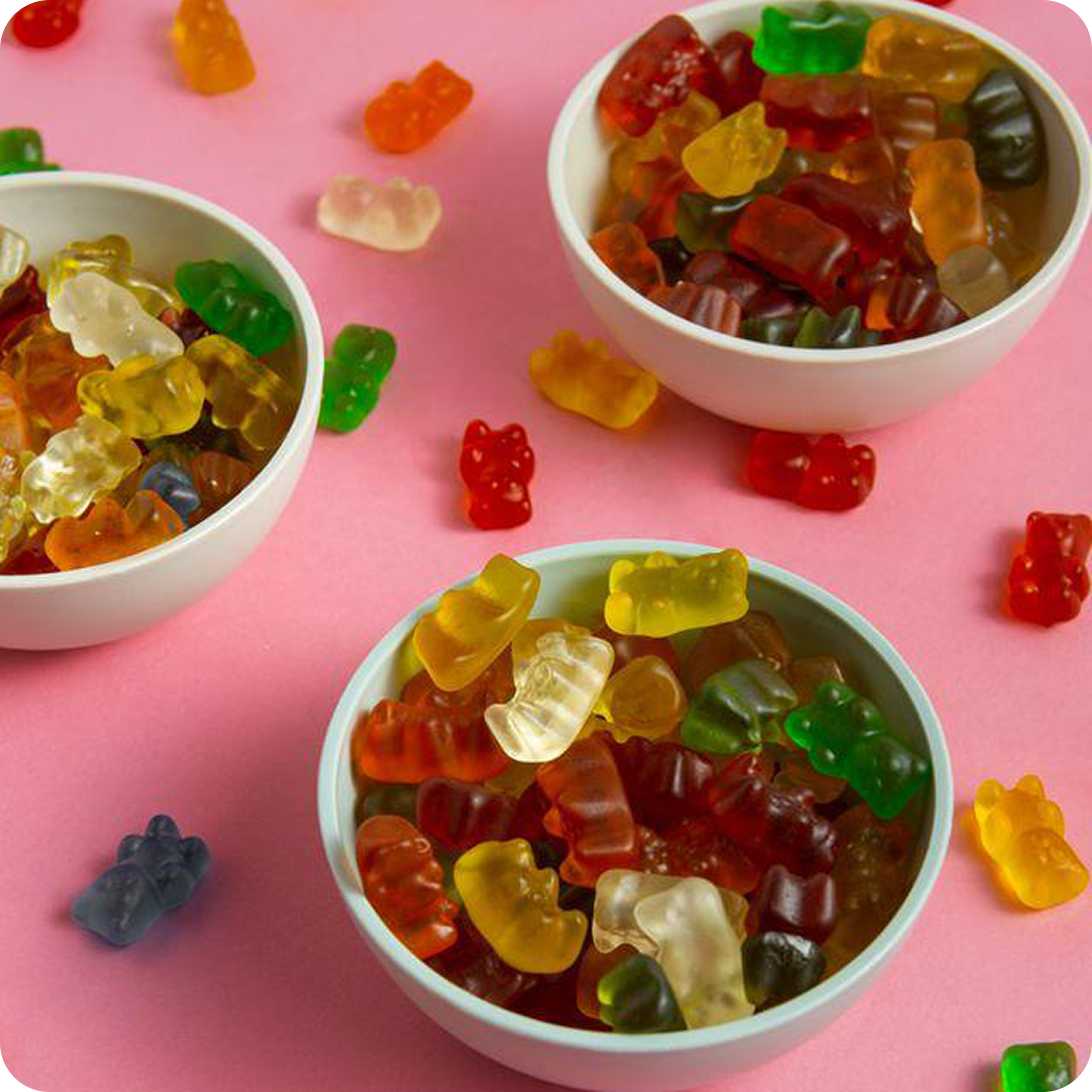 Bowls of colorful gummy bears on a pink background.