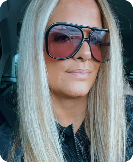 Person with long blonde hair and large sunglasses in a car.