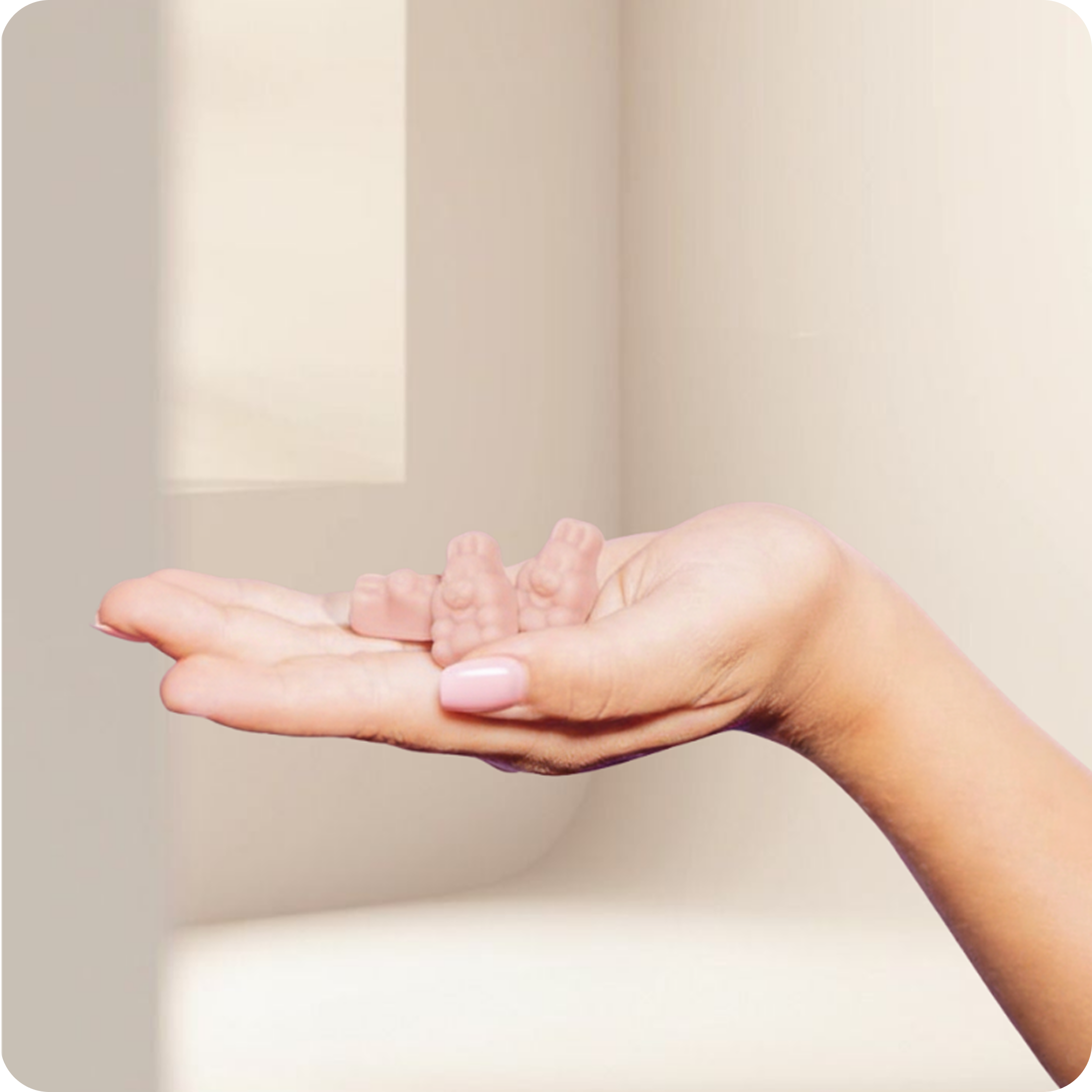 A hand holding two small, pink, gummy bear-like figures.