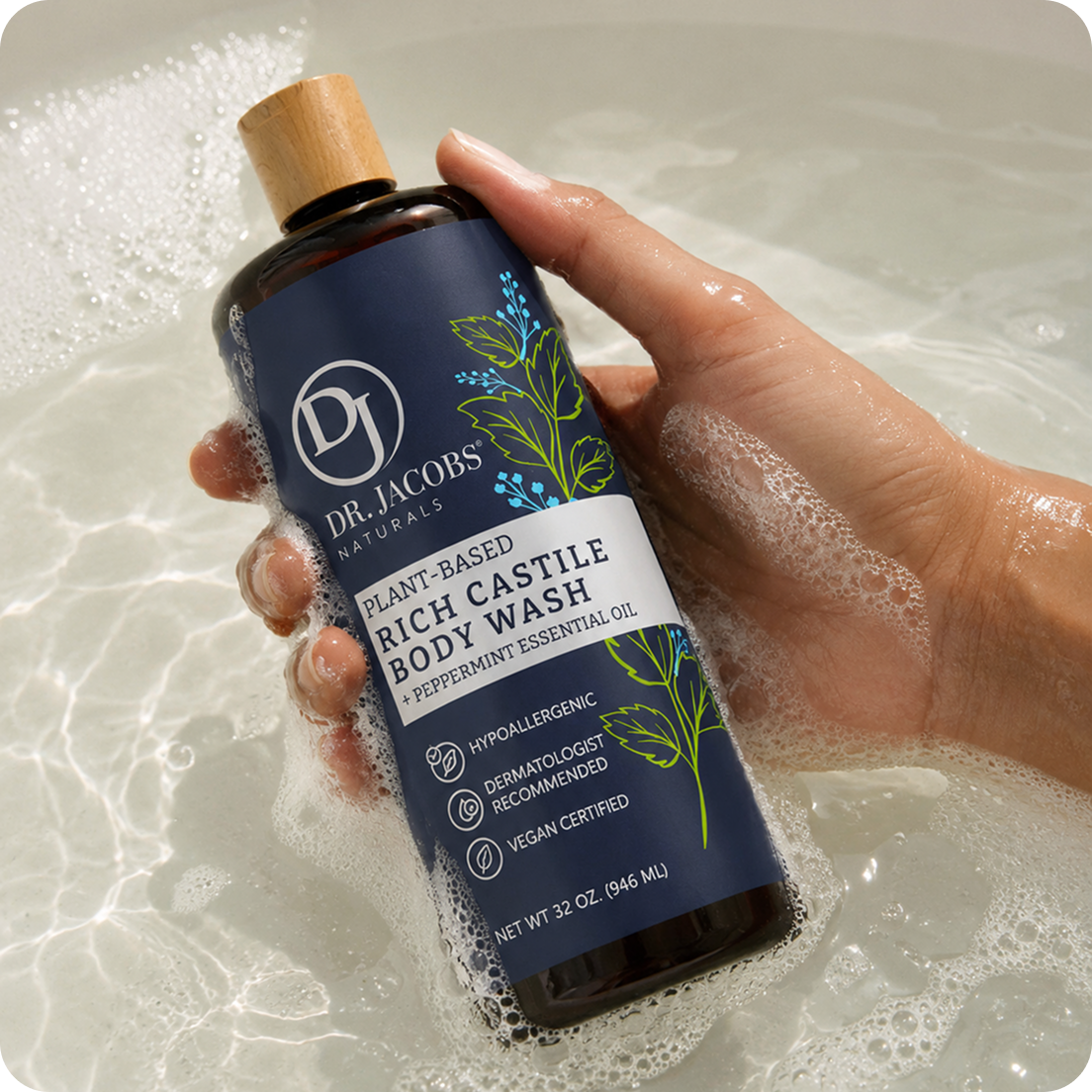 A hand holds a bottle of Dr. Jacobs Naturals body wash in a bubbly bath.