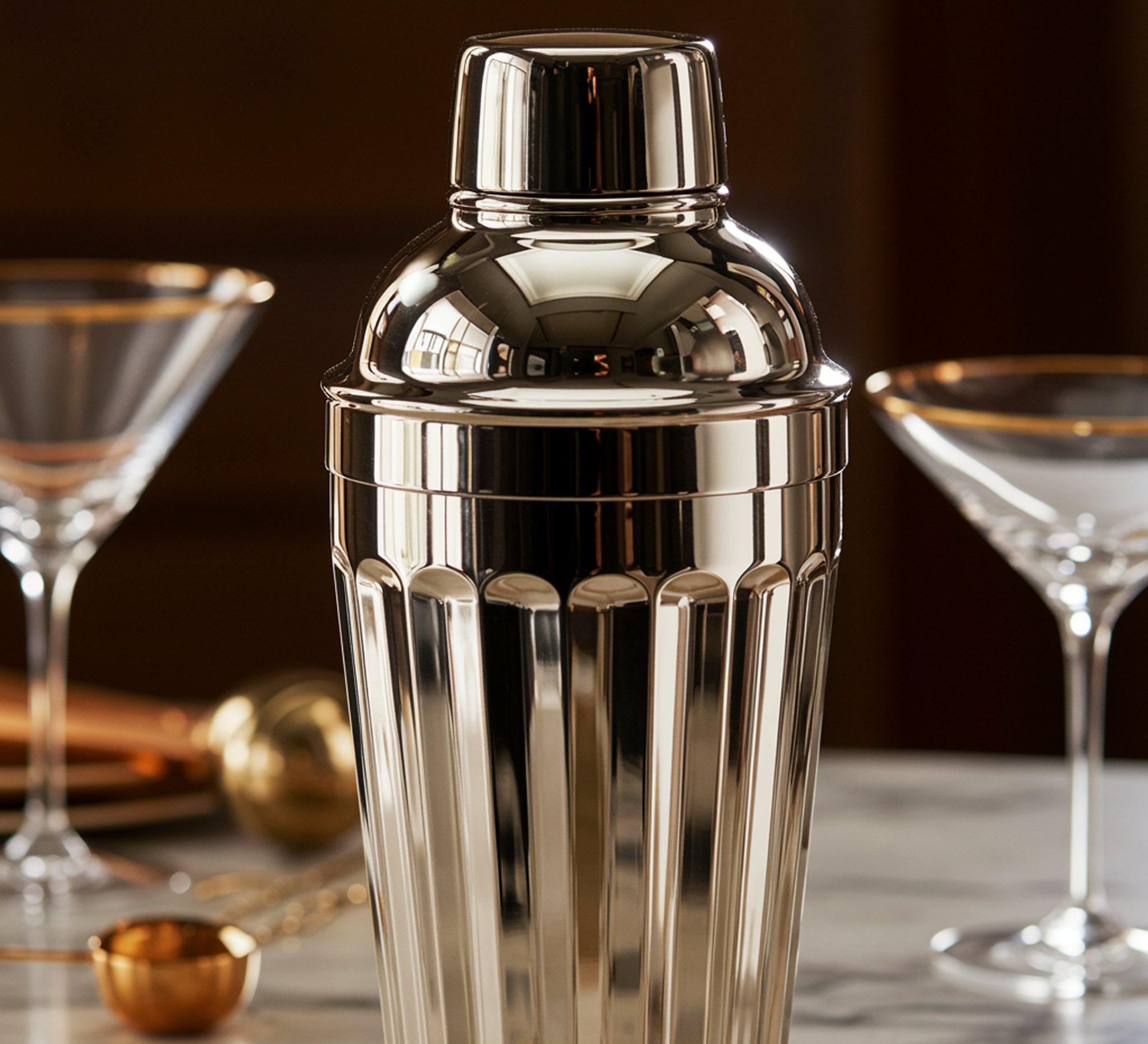 Silver cocktail shaker with martini glasses on a marble surface.