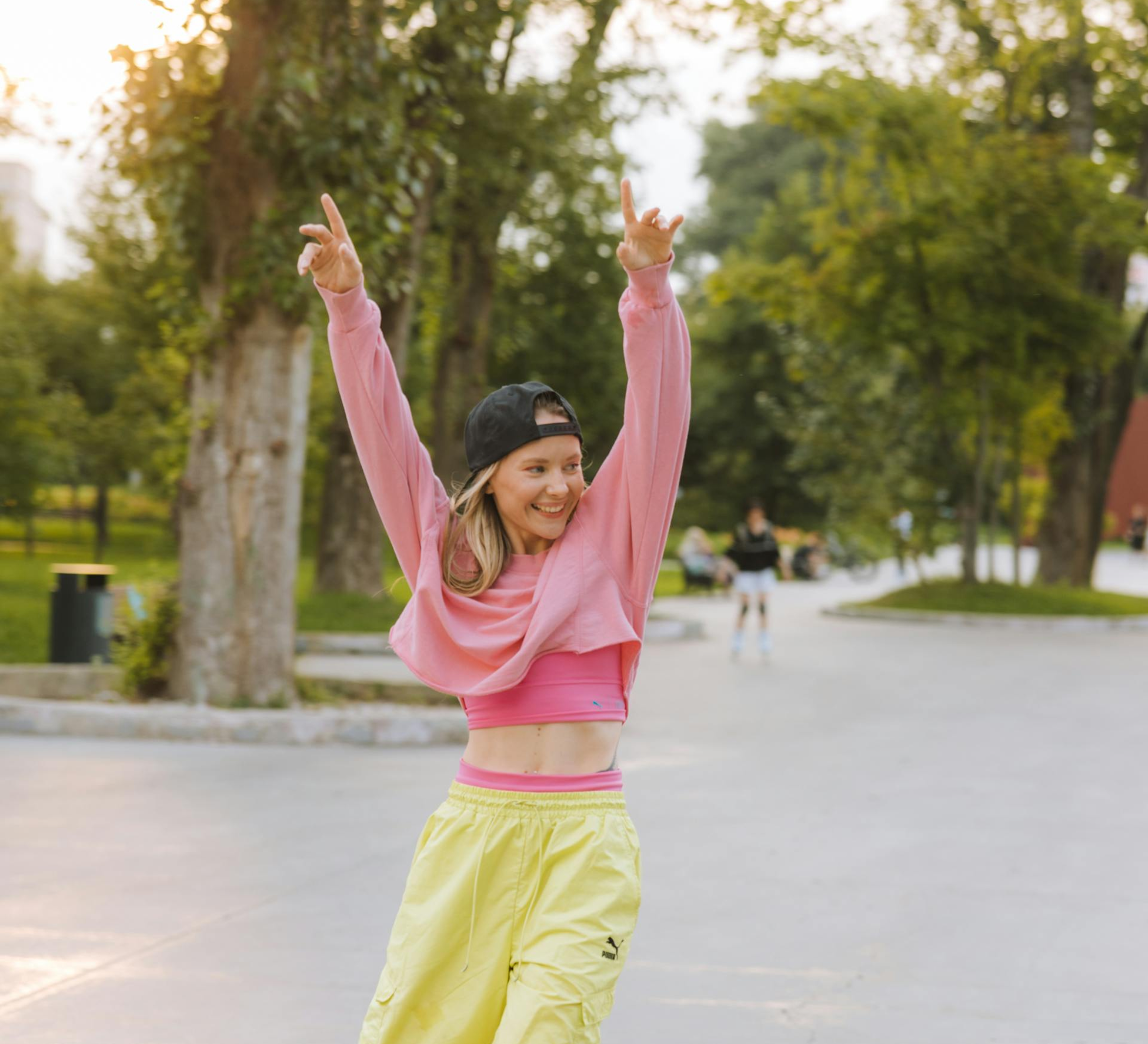 Person in pink top and yellow pants dancing outdoors.