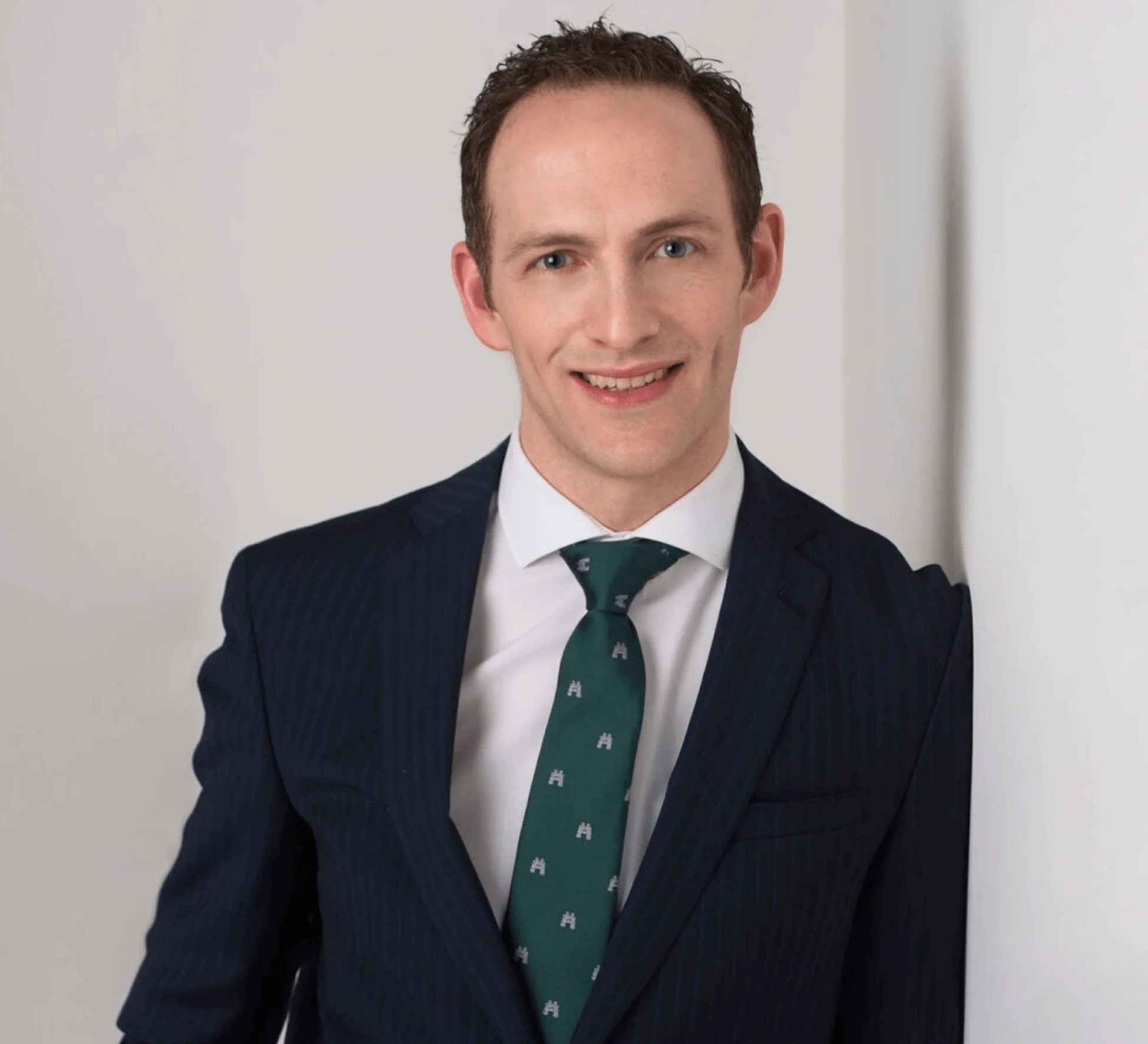 Man in a suit with a green tie, smiling against a white background.