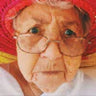 Elderly person wearing glasses and a red hat, looking directly at the camera.