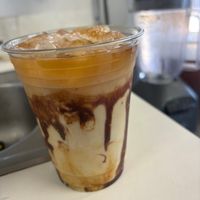 Iced coffee with cream and caramel in a clear plastic cup.