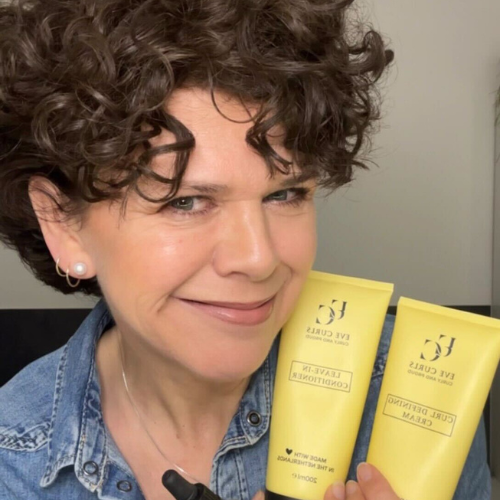 Person holding two yellow haircare bottles, smiling, wearing a denim shirt.