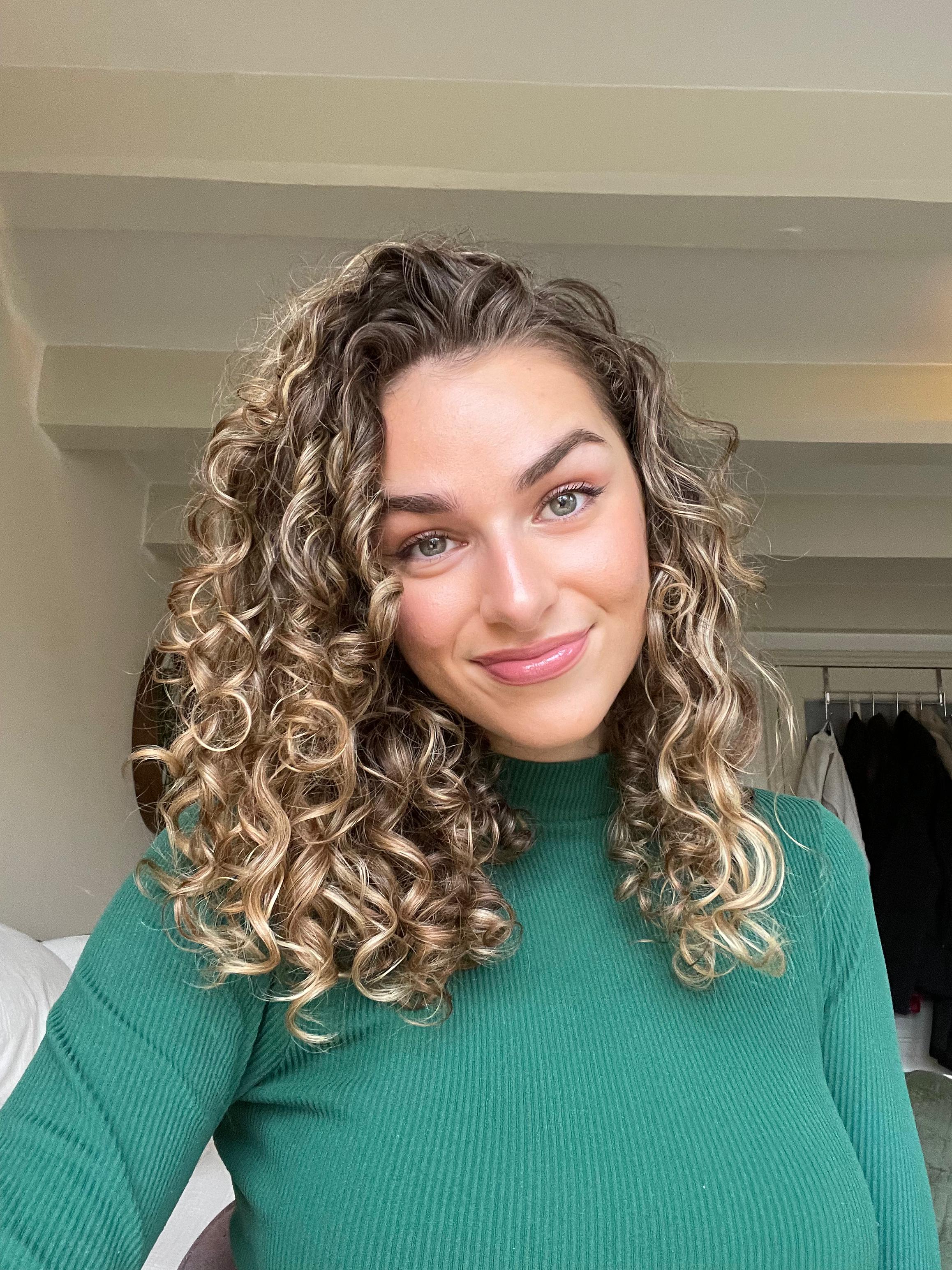 Person with curly hair wearing a green top, standing indoors.