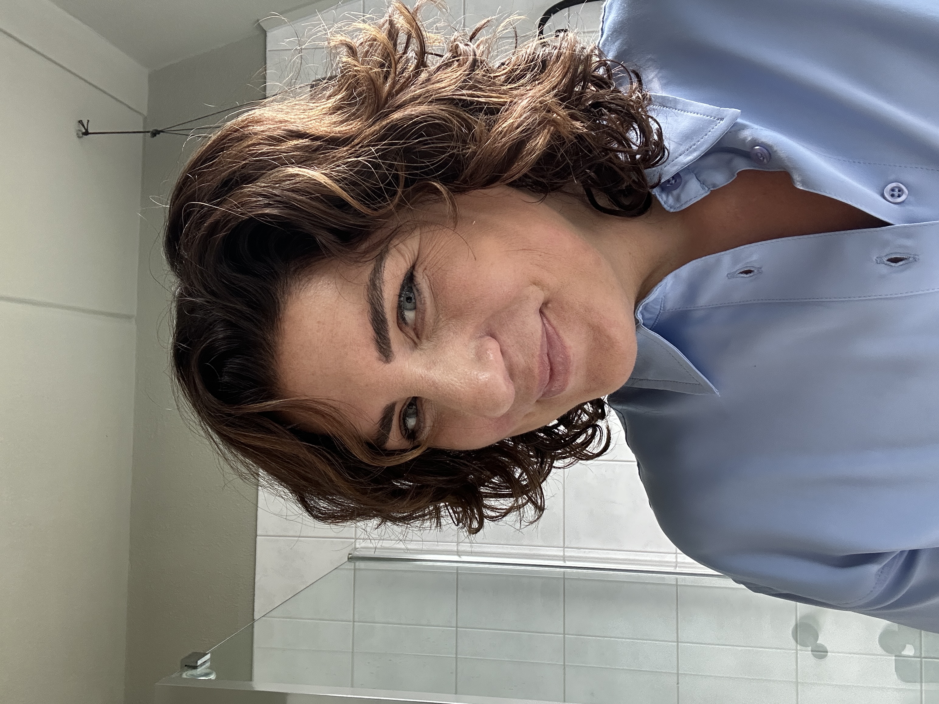 Person with curly hair smiling in a bright room.