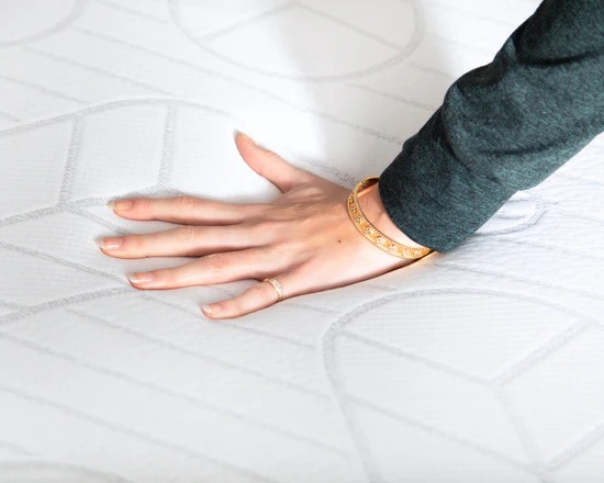 A person's hand with a gold bracelet pressing down on a white, quilted mattress.
