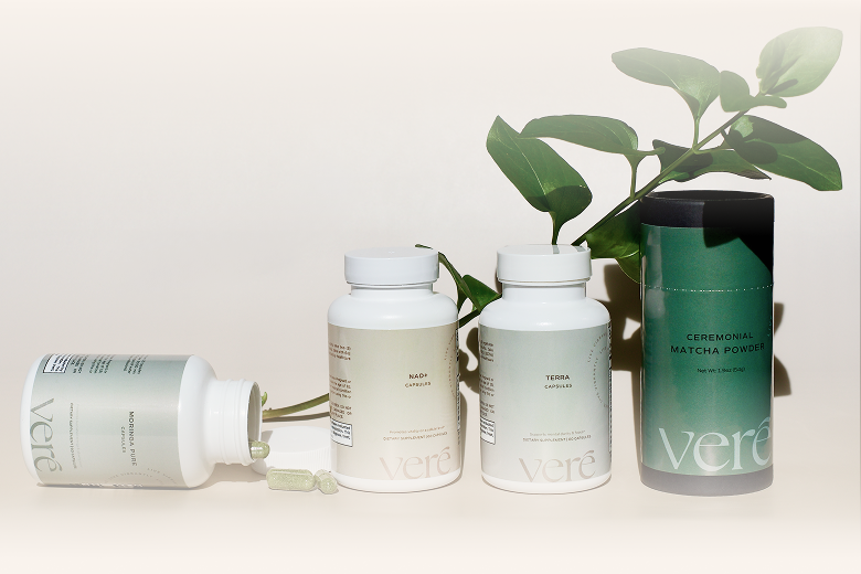 Three bottles of Veré supplements arranged amongst fresh vegetables like kale, tomatoes, and mushrooms.