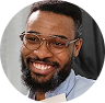 A smiling Black man with a beard and glasses in a circular cropped photo.
