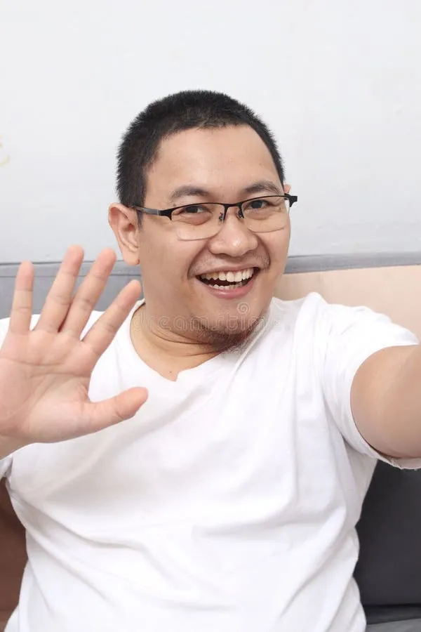 A smiling man with glasses and a white shirt waving at the camera.