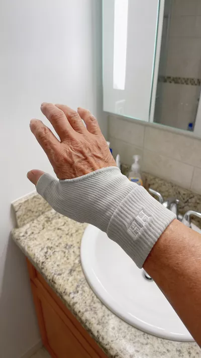 Hand wearing a grey compression glove with thumbhole over a bathroom sink.