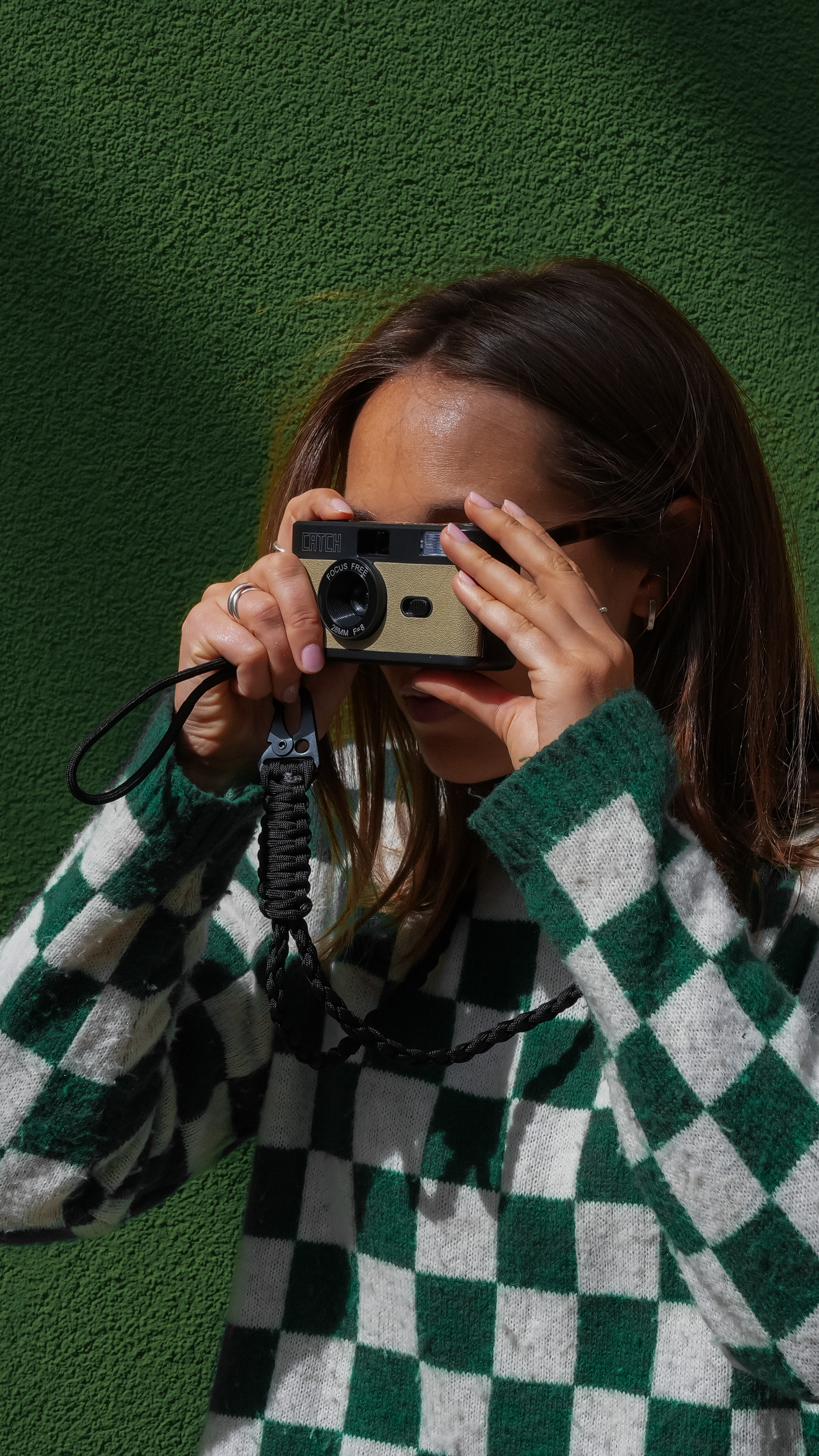 Person holding a camera against a green textured wall.