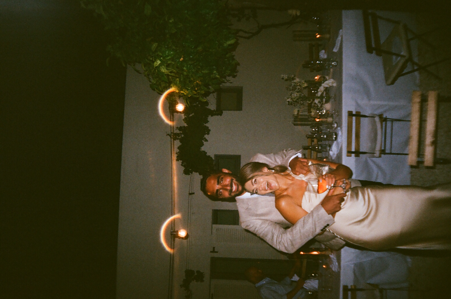 Smiling couple embracing at an outdoor evening event with string lights.