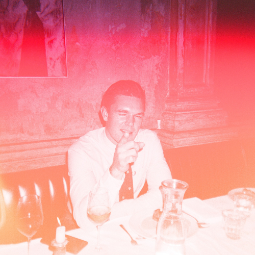 Man in formal attire sitting at a restaurant table with a red light overlay.